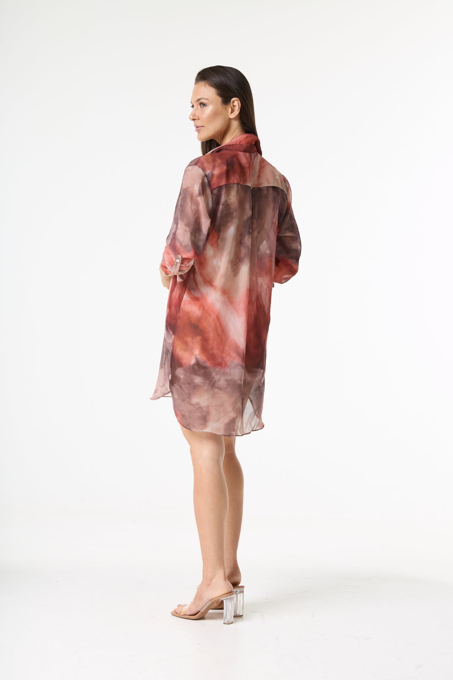 Chemise longa estampada aquarela transparente em tons de marrom e terracota. A modelo está de costas, virada de lado, exibindo o caimento solto da peça sobre um fundo branco.
