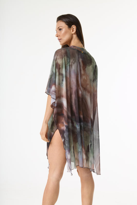 Saída de praia kaftan com estampa abstrata em tons de verde, marrom e roxo. A modelo é vista de costas, virando o rosto de perfil, exibindo o caimento esvoaçante da peça com fenda lateral em fundo branco.