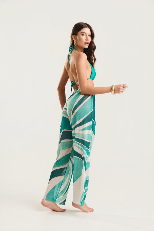 Calça pantalona estampada verde e branca, modelo de costas em postura de três quartos com leve torção do tronco