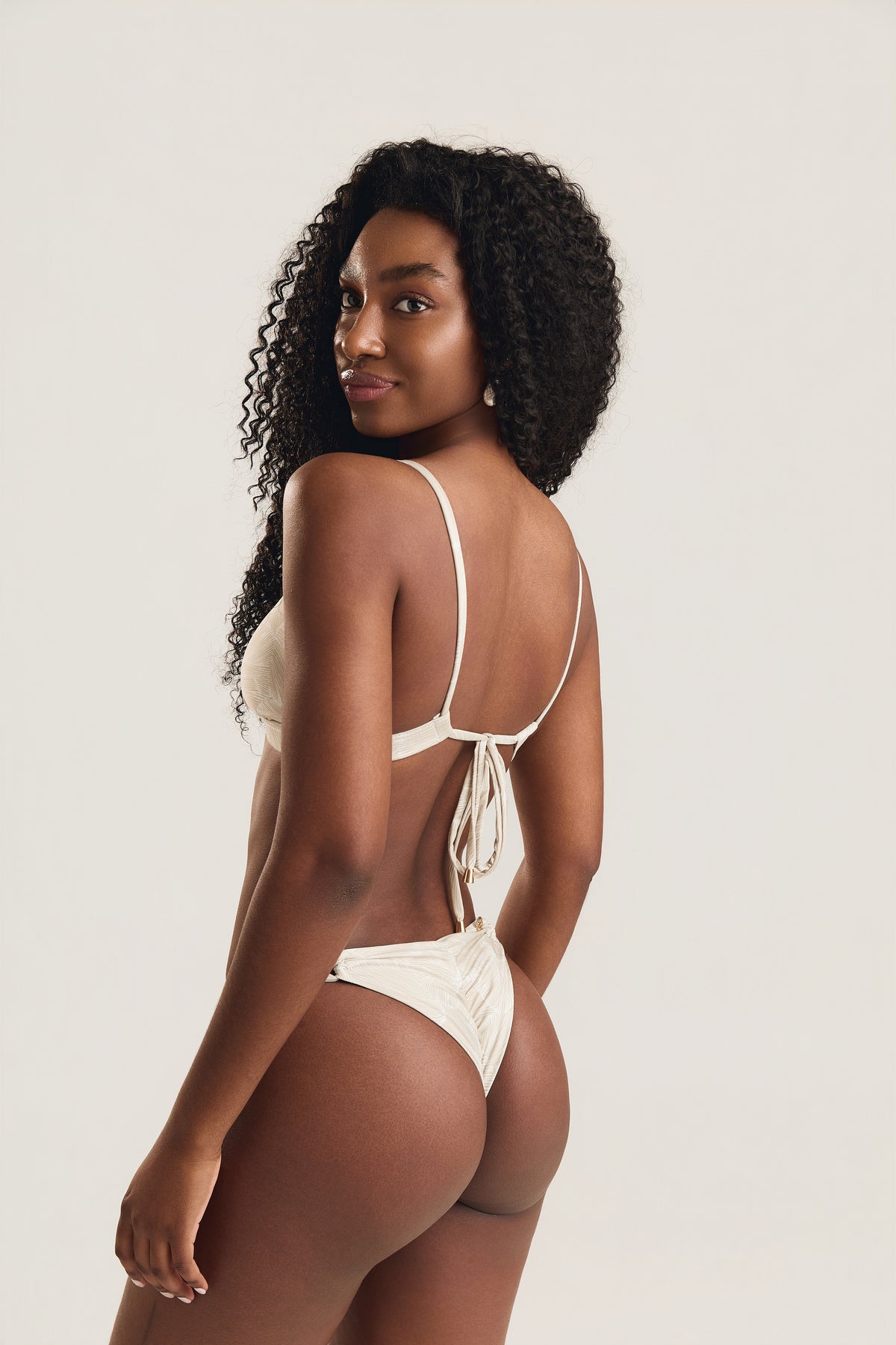 Top metal coral e calcinha roletê duplo conchas off white, modelo em posição de costas com leve giro e sorriso, mostrando o amarrado das alças
