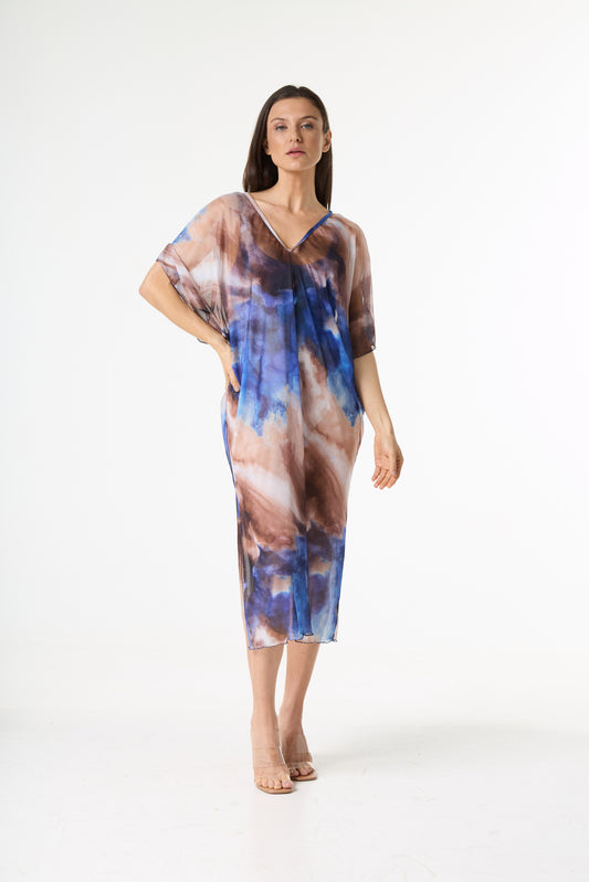 Vestido kaftan estampa abstrata azul marrom, com decote em V e tecido levemente transparente. A modelo está de pé em um fundo branco, com uma mão na cintura, mostrando o caimento fluído da peça.