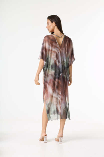 Vestido kaftan longo estampado. Modelo de costas, olhando por cima do ombro esquerdo, veste a peça transparente com estampa abstrata em tons de marrom, verde e toques de cinza