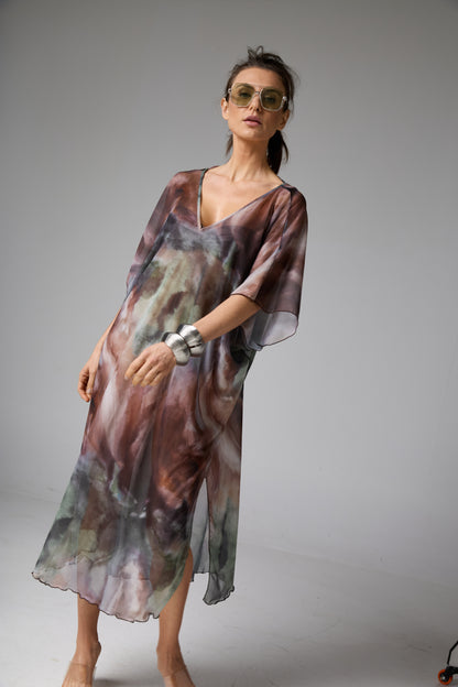 Vestido kaftan com estampa aquarelada em tons de marrom, verde e cinza. A modelo usa óculos de sol e bracelete, posando de frente, realçando o caimento solto e elegante da peça.