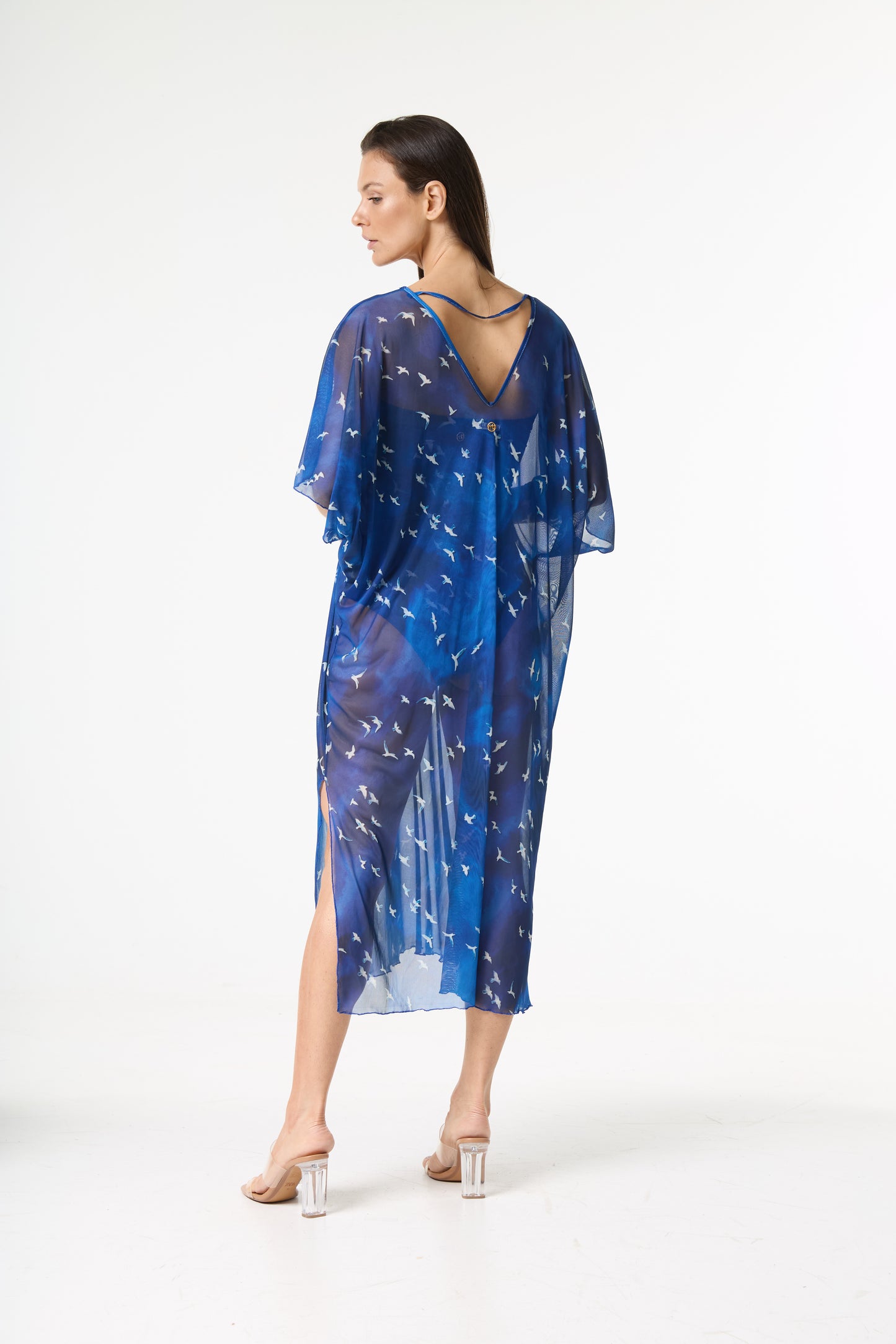 Saída de praia kaftan azul com estampa de pássaros brancos. A modelo posa de costas, olhando para a esquerda, exibindo o decote V e o