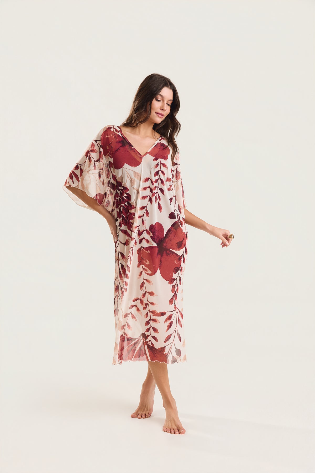 Kaftan Tule Mareblu em tule floral com estampa de flores e folhagens — modelo de frente, olhar direcionado para baixo, braço levemente afastado do corpo