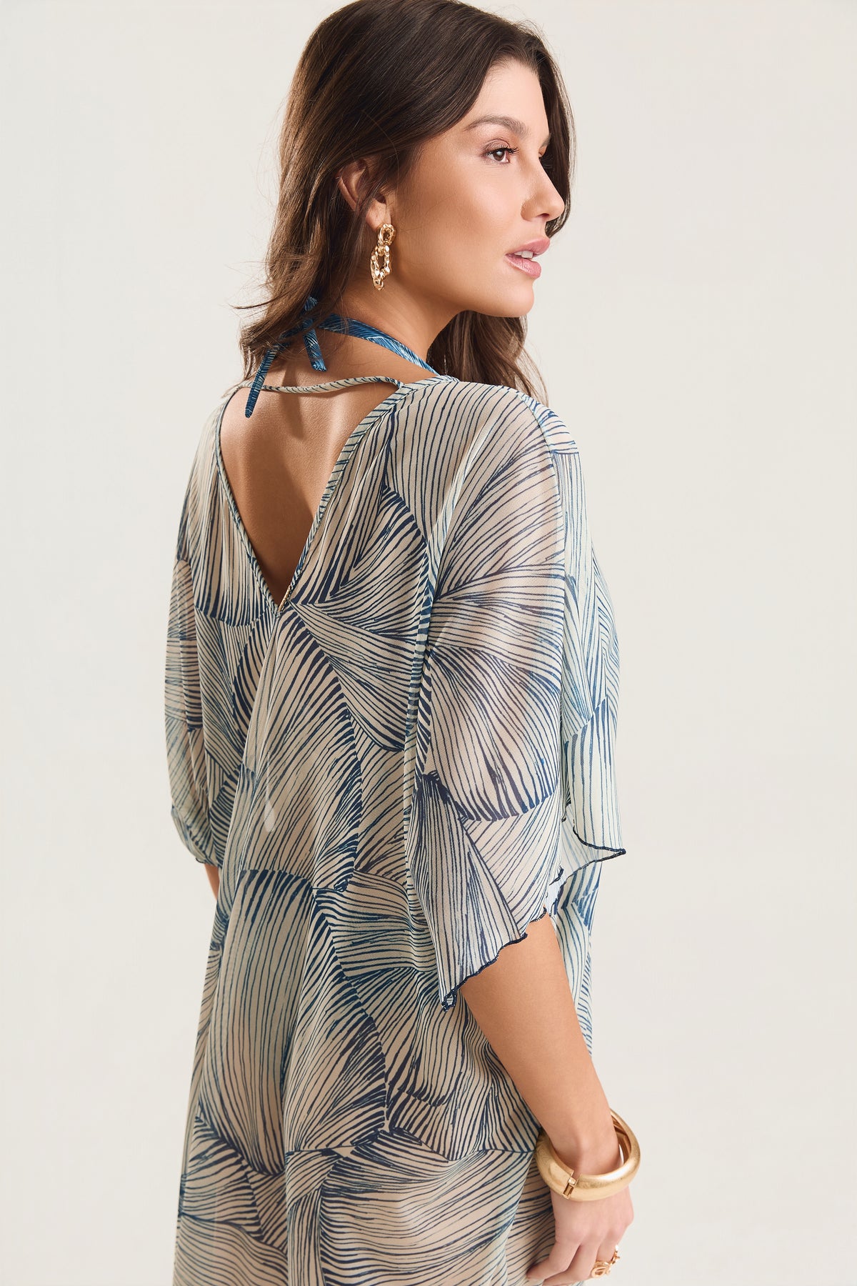 Kaftan Tule Mareblu em tule com estampa concha azul — detalhe do decote V profundo nas costas, modelo em ¾ com acessórios dourados