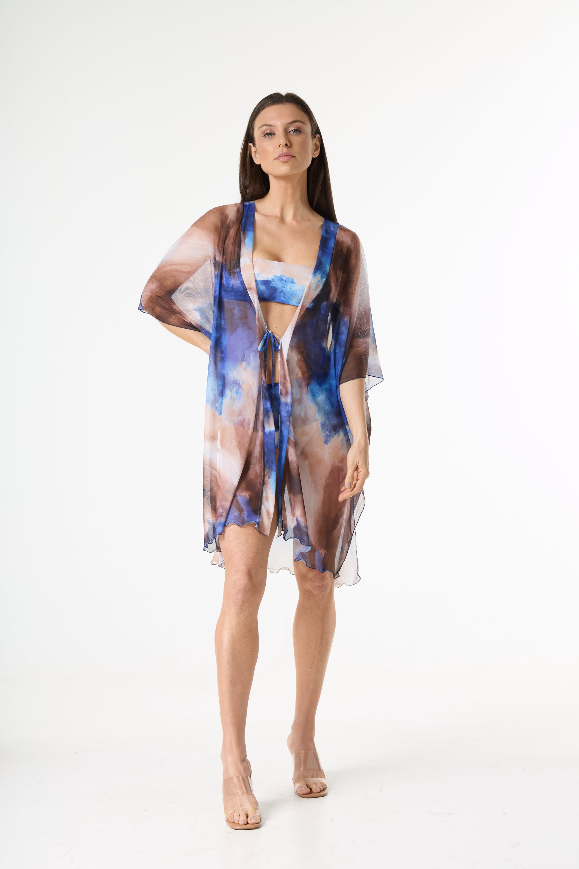 Saída de praia quimono com estampa abstrata em tons de azul e marrom. A modelo está de frente, de corpo inteiro, em estúdio branco, exibindo a peça que inclui um quimono transparente de mangas largas e um biquíni bandeau com a mesma estampa.