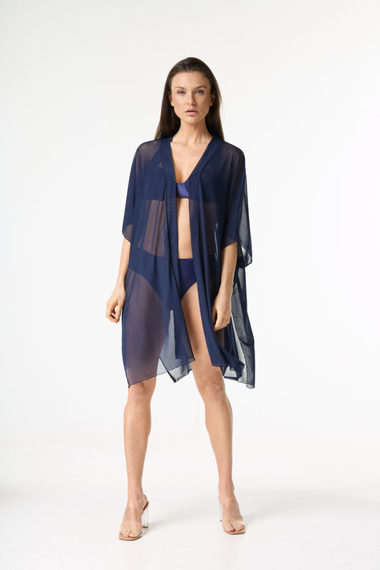 Saída de praia kaftan azul marinho. A modelo posa de frente em um fundo branco, vestindo a peça transparente sobre um biquíni azul marinho, destacando o caimento solto.