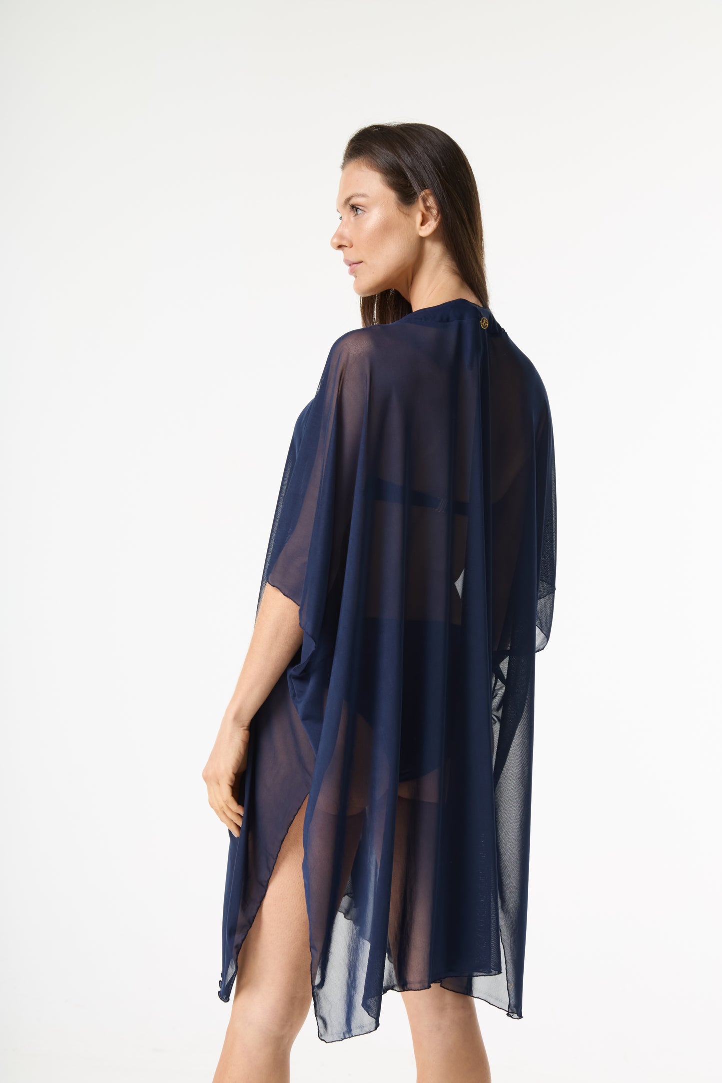 Saída de praia kaftan azul marinho. A modelo está de costas, virada de lado, mostrando o caimento fluido e translúcido da peça com mangas largas sobre um biquí