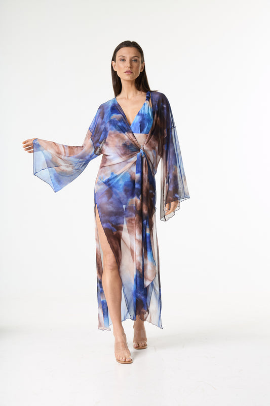 Saída de praia longa amarração estampa abstrata. A modelo está de pé, de frente, em fundo branco, exibindo a peça de tecido transparente com estampa tie-dye