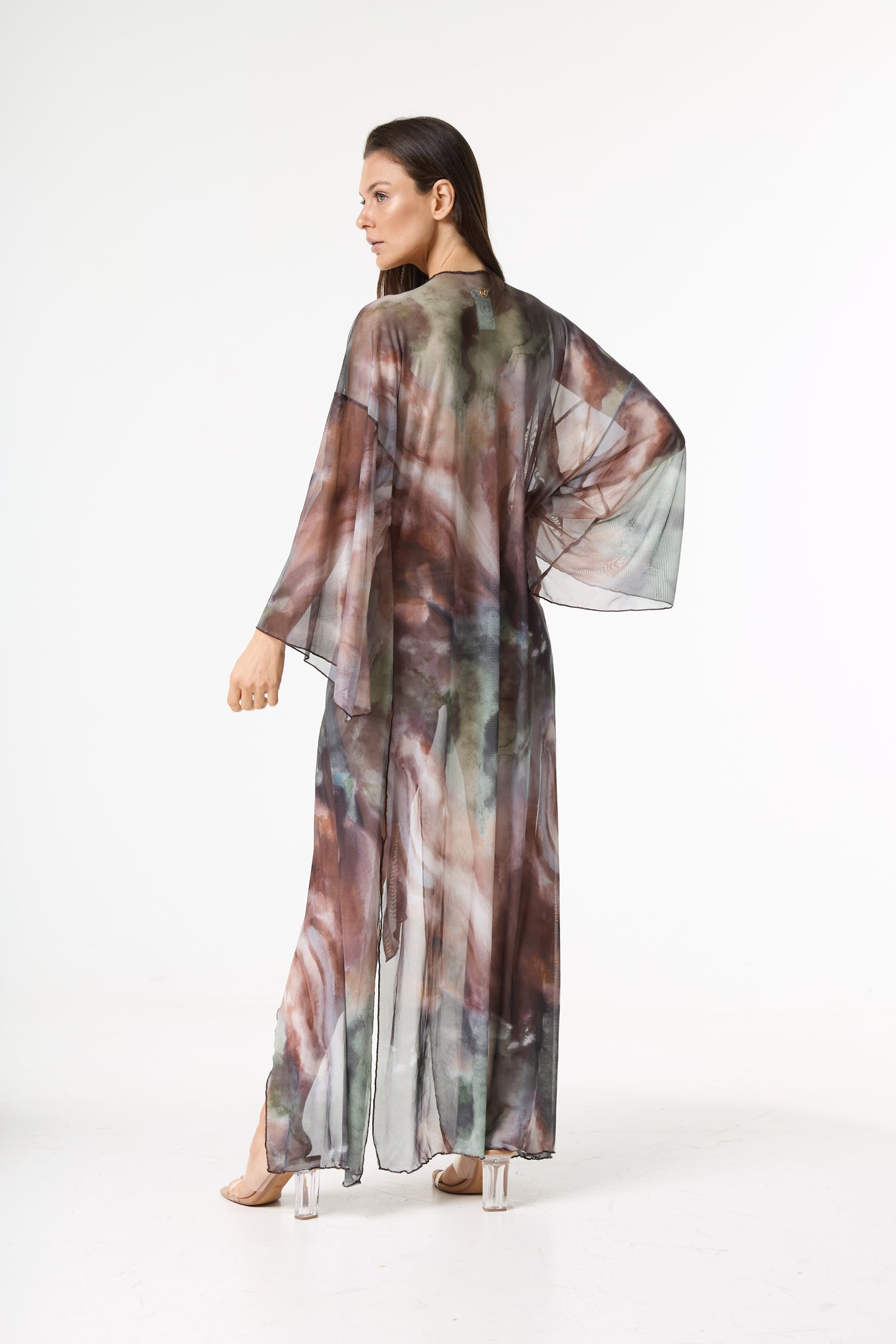 Saída de praia longa com estampa aquarelada em tons de marrom, verde e cinza. A modelo está de costas, virada de lado e olhando por cima do ombro, destacando o caimento fluido da peça.