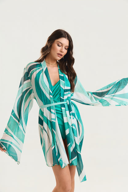 Kimono de manga longa com estampgeo verde amarrado na cintura, modelo em posição frontal com olhar direcionado para baixo e manga aberta ao vento
