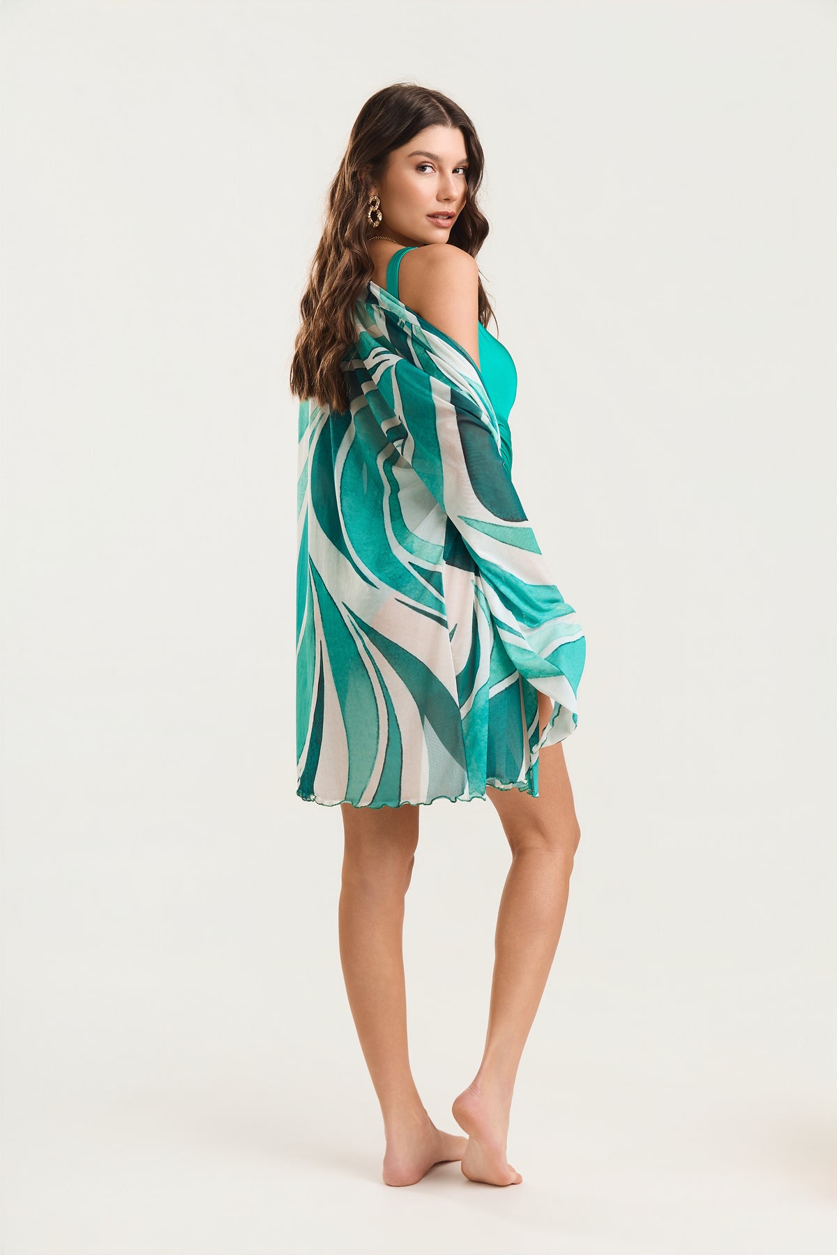 Kimono de manga longa com estampageo verde visto de costas, modelo em posição de três quartos olhando por cima do ombro, com fluido ao vento
