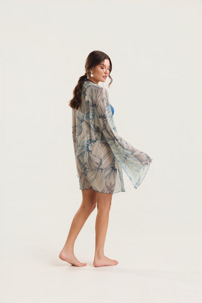 Kimono de manga longa com estampa de conchas azuis visto de costas, modelo em posição de perfil caminhando, com o tecido fluido ao vento
