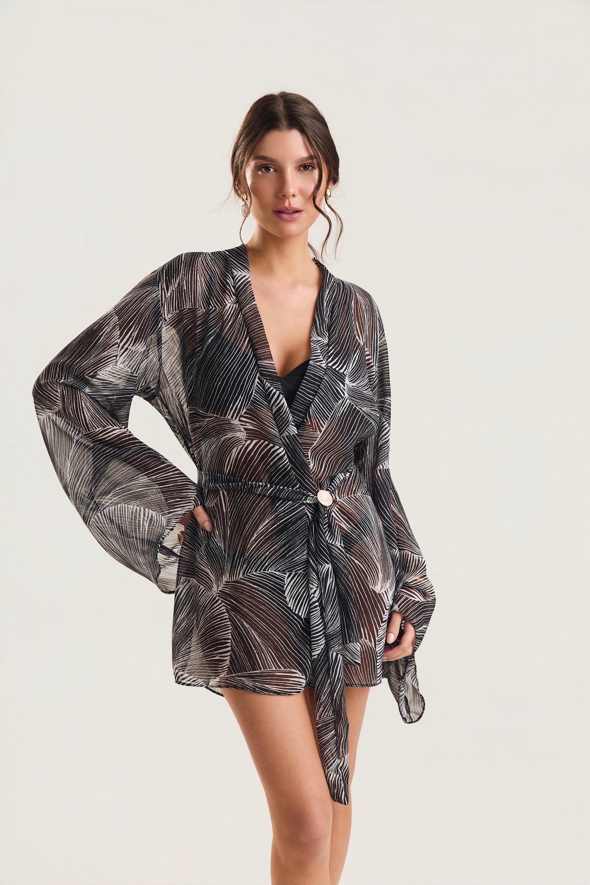 Kimono de manga longa com estampa de conchas pretas, modelo em posição frontal com mão na cintura, destacando o cinto e o decote aberto

