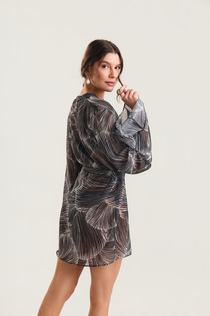 Kimono de manga longa com estampa deconchas pretas visto de costas, modelo em posição de três quartos olhando por cima do ombro, com mão levantada próxima ao rosto

