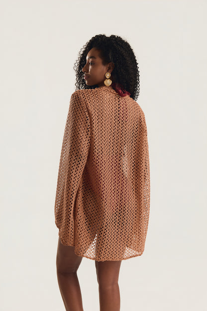 Kimono de manga longa emcrochê caramelo visto de costas, modelo em posição de três quartos olhando por cima do ombro, com maiô vinho aparente através do tecido vazado 