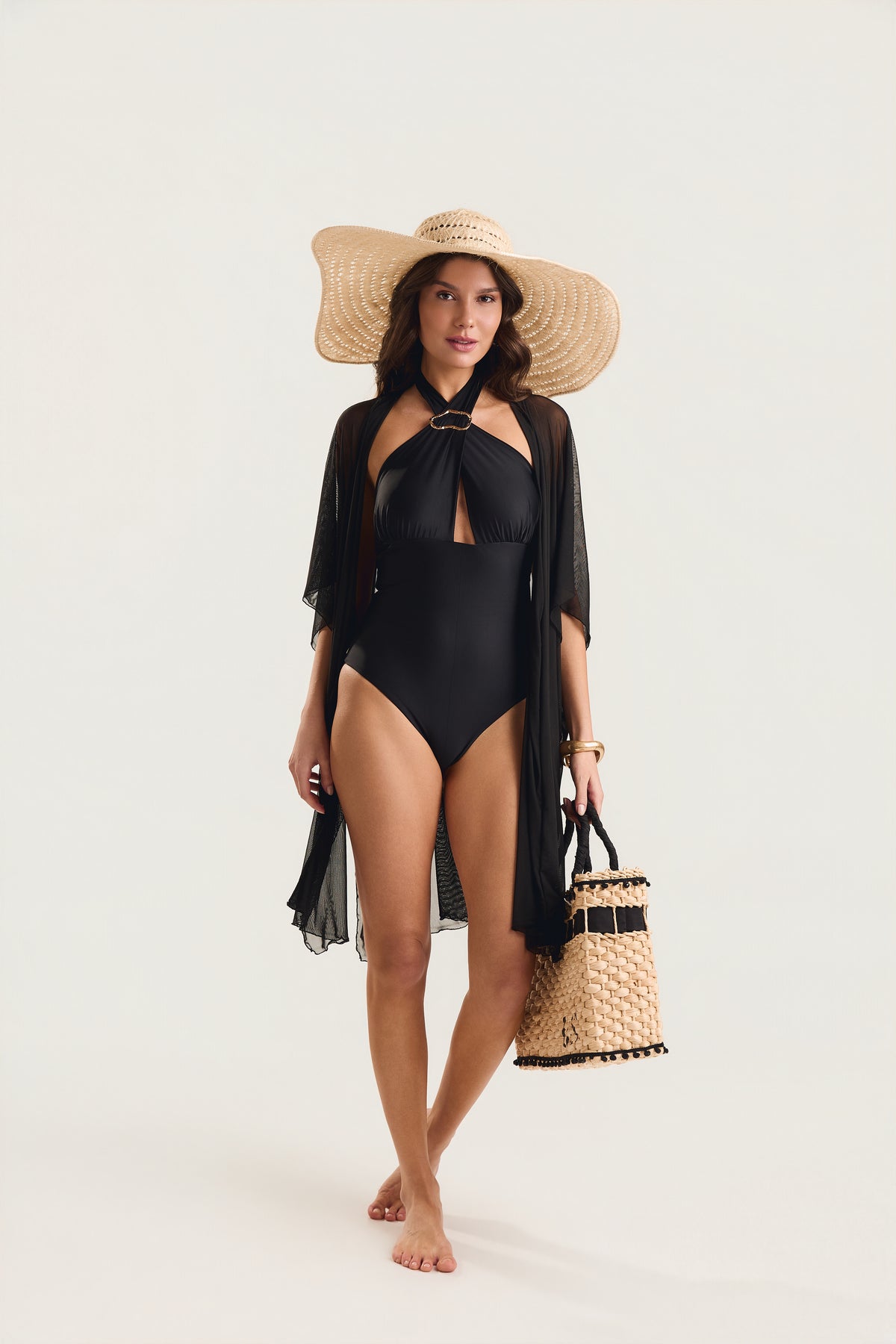 Modelo em posição frontal caminhando, usando maiô preto com decote halter e argola dourada
