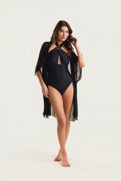 Modelo com mão no cabelo, usando maiô preto com decote halter e argola dourada
