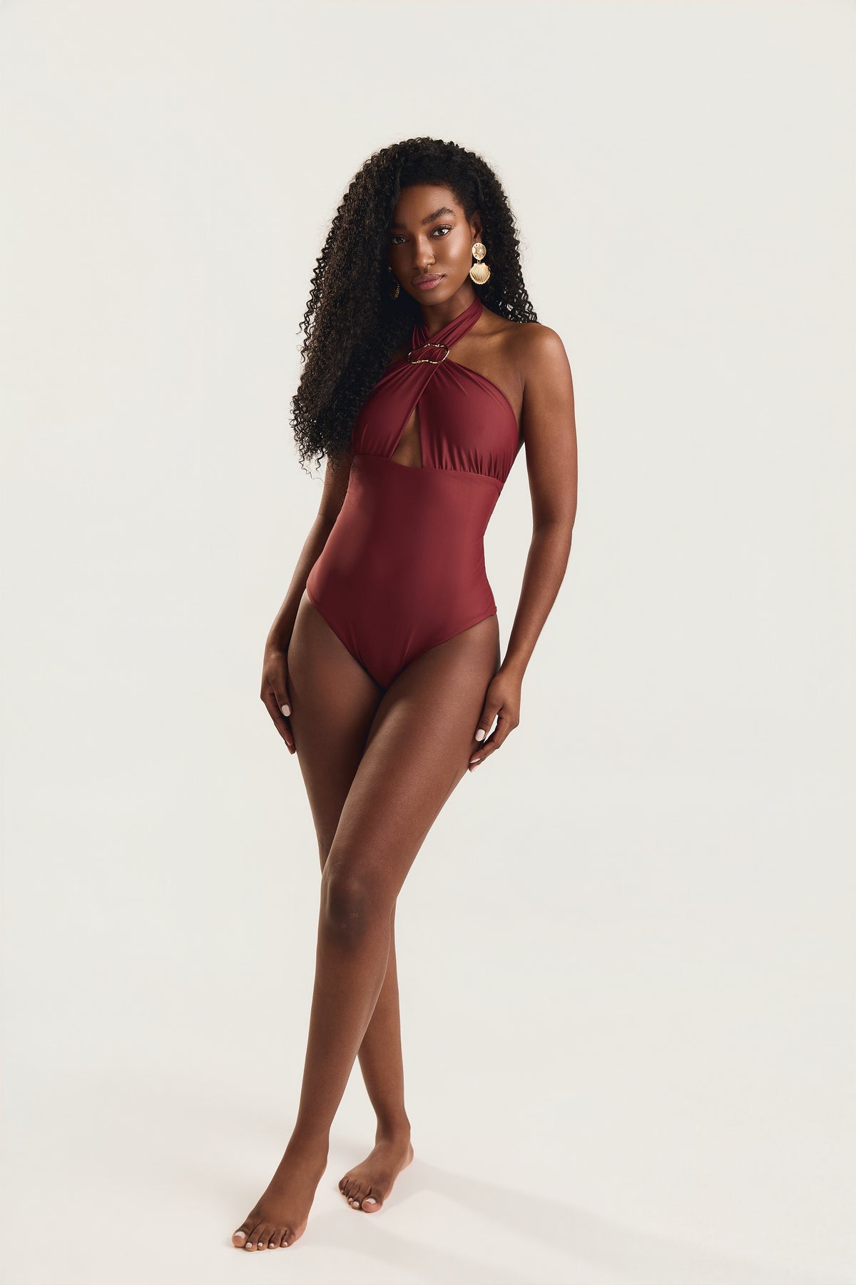 Modelo em posição frontal com pernas cruzadas e olhar para a câmera, usando maiô siena liso com decote halter cruzado
