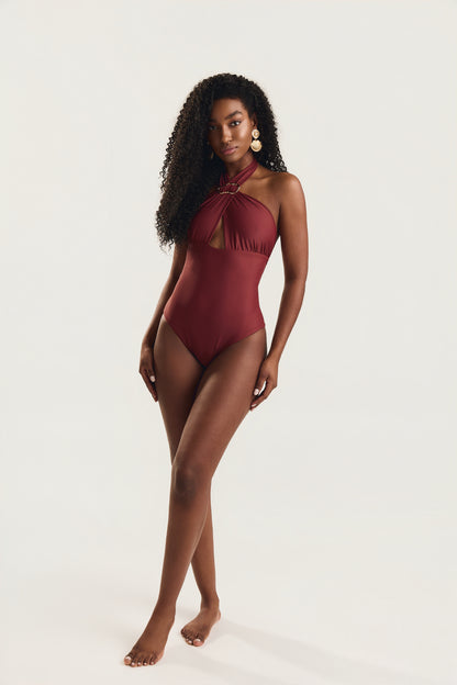 Modelo em posição frontal com pernas cruzadas e olhar para a câmera, usando maiô siena liso com decote halter cruzado
