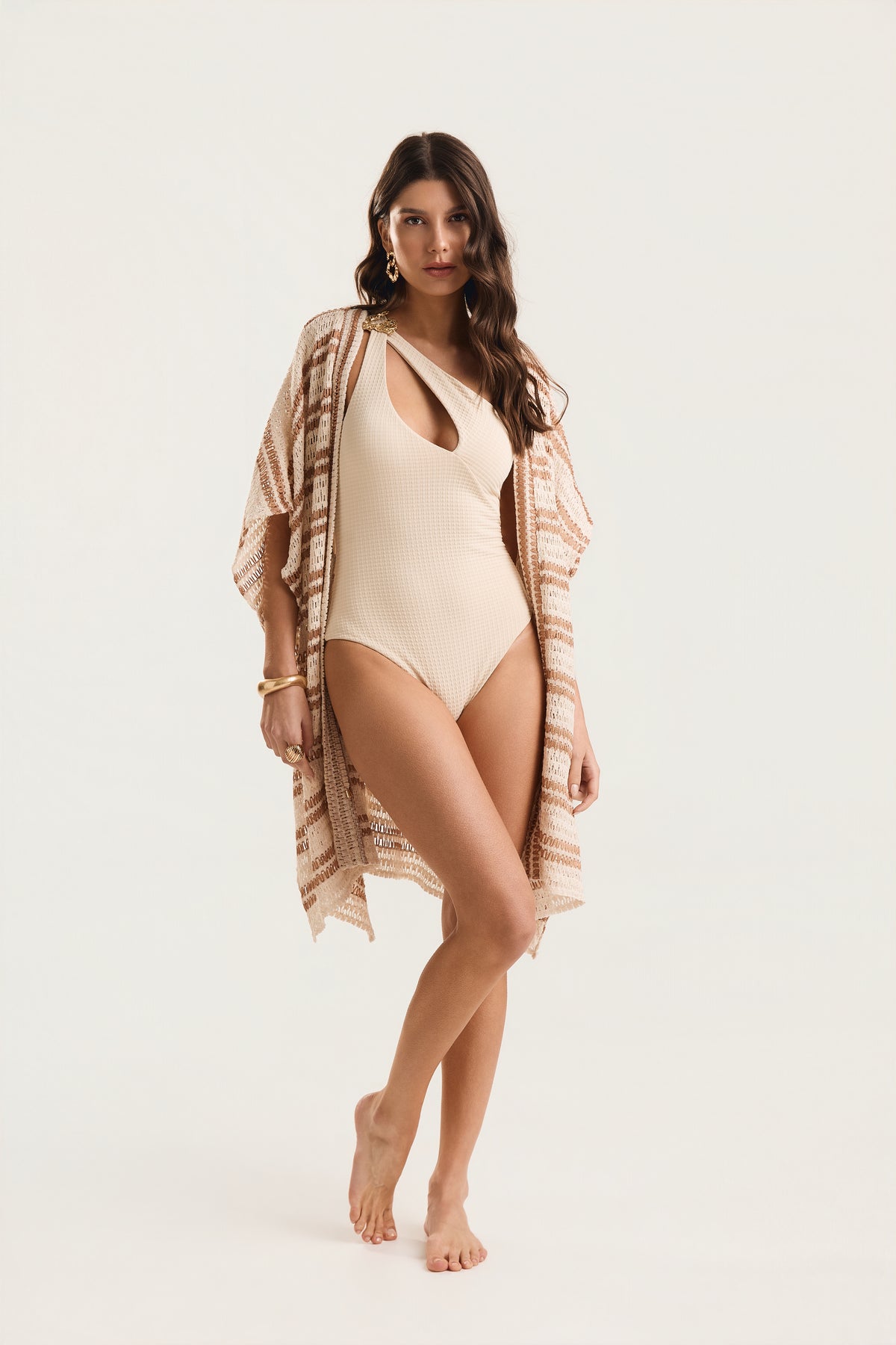 Maiô Um Ombro Metal Amassado off white textura, modelo em pose frontal com perna cruzada à frente, usando saída de praia kimono estampada em tons terrosos, fundo neutro claro.

