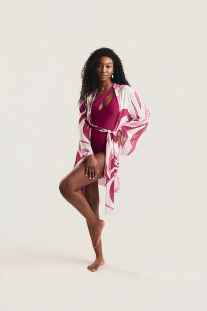 Maiô Um Ombro Metal Amassado carmim, modelo em pose frontal com joelho levantado e kimono estampado em geo rosa e branco amarrado na cintura, olhar direto para a câmera, fundo neutro claro.