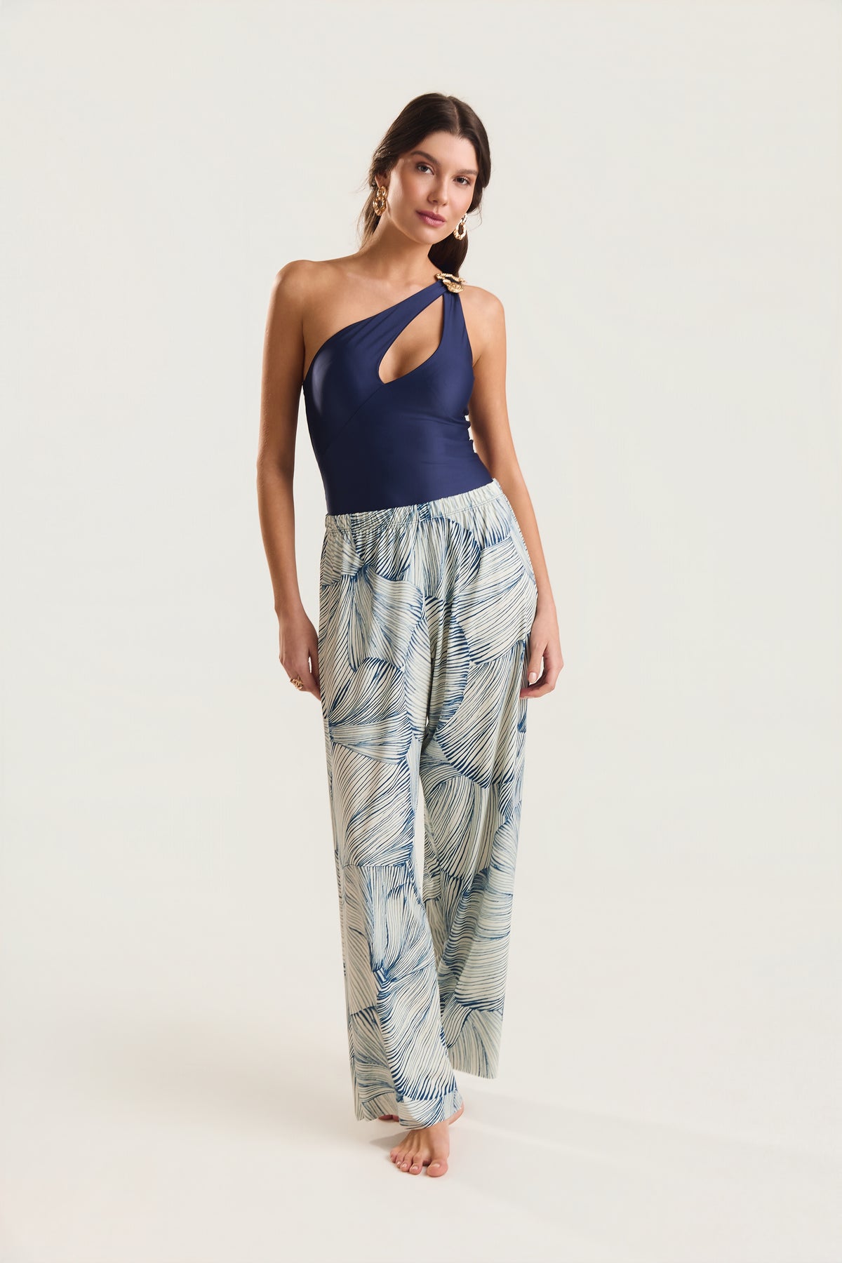 Calça pantalona estampada em azul e off-white com estampa de conchas azuis, modelo em postura frontal com posição relaxada dos braços