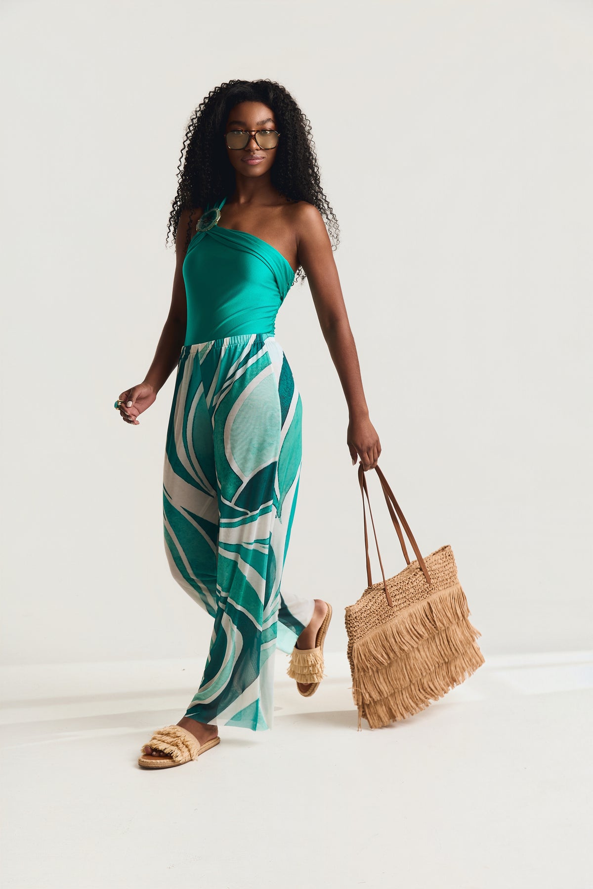 Maiô Um Ombro Pedra Detalhe Franzido Mareblu na cor jade, modelo caminhando de frente usando pantalona geo verde e segurando bolsa de palha com franjas
