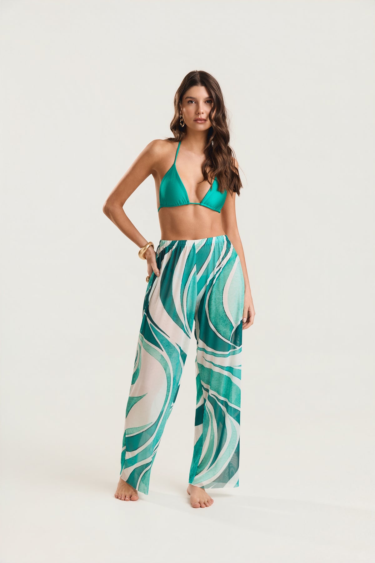 Calça pantalona estampada em tons de verde e branco com estampa fluida, modelo em postura frontal com uma mão na cintura