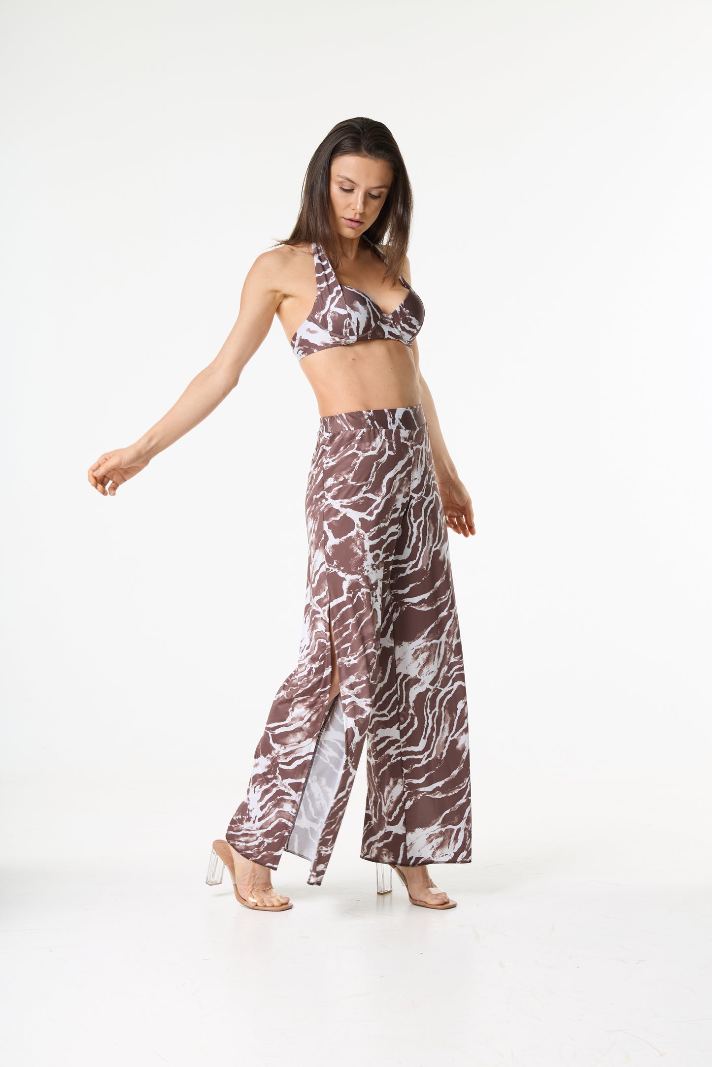 Conjunto biquíni calça marmorizada marrom e branca. A modelo está de pé em fundo branco, olhando para baixo, com o corpo ligeiramente inclinado, exibindo