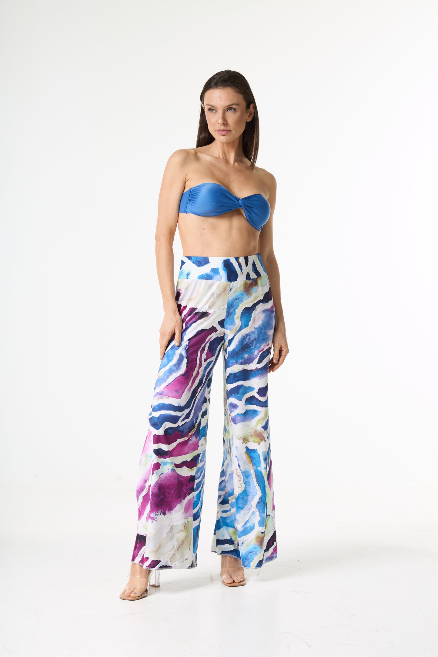 Conjunto com top faixa azul e calça pantalona de estampa aquarelada em tons de azul, roxo e rosa. A modelo posa de pé em fundo branco, exibindo