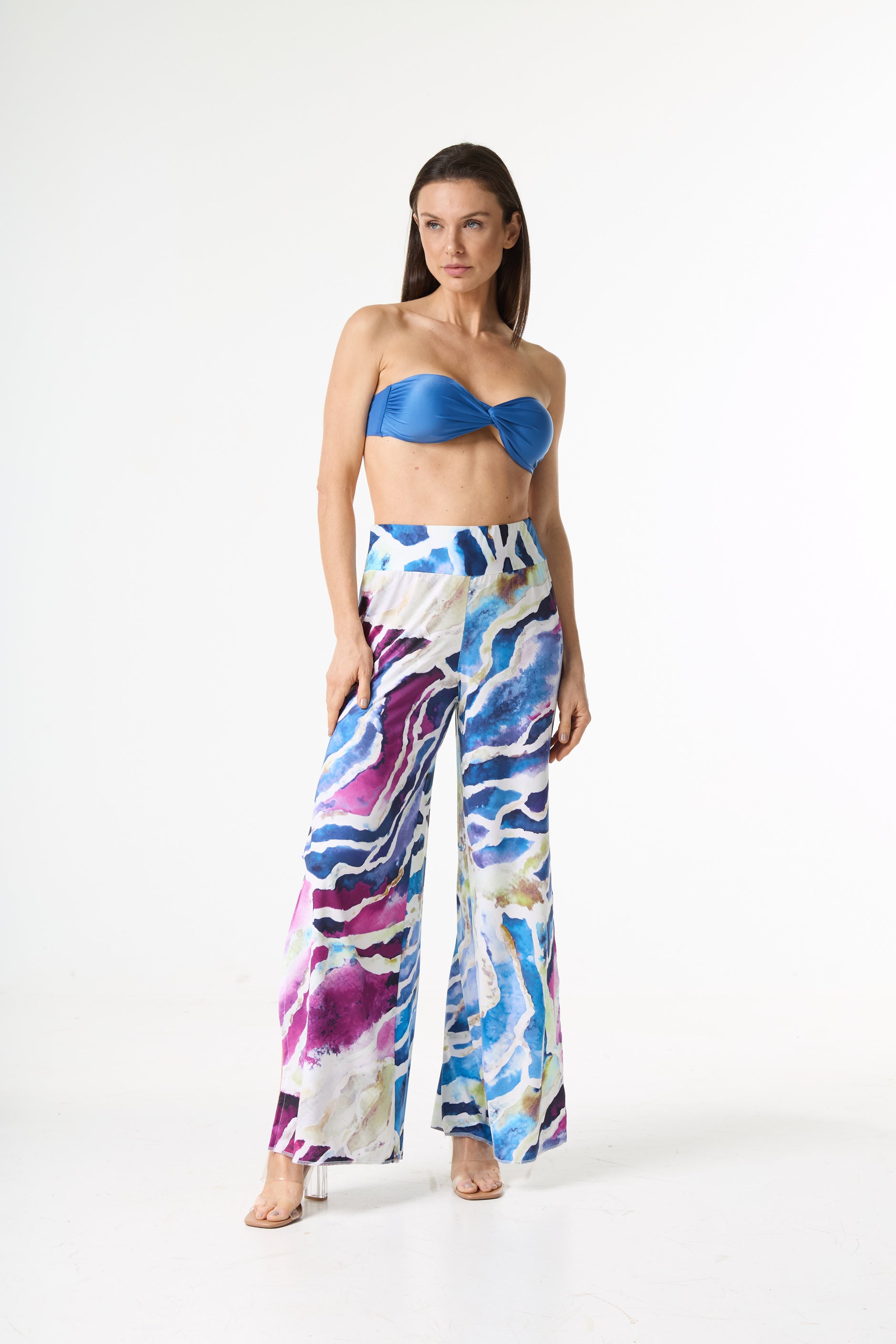 Conjunto com top faixa azul e calça pantalona de estampa aquarelada em tons de azul, roxo e rosa. A modelo posa de pé em fundo branco, exibindo