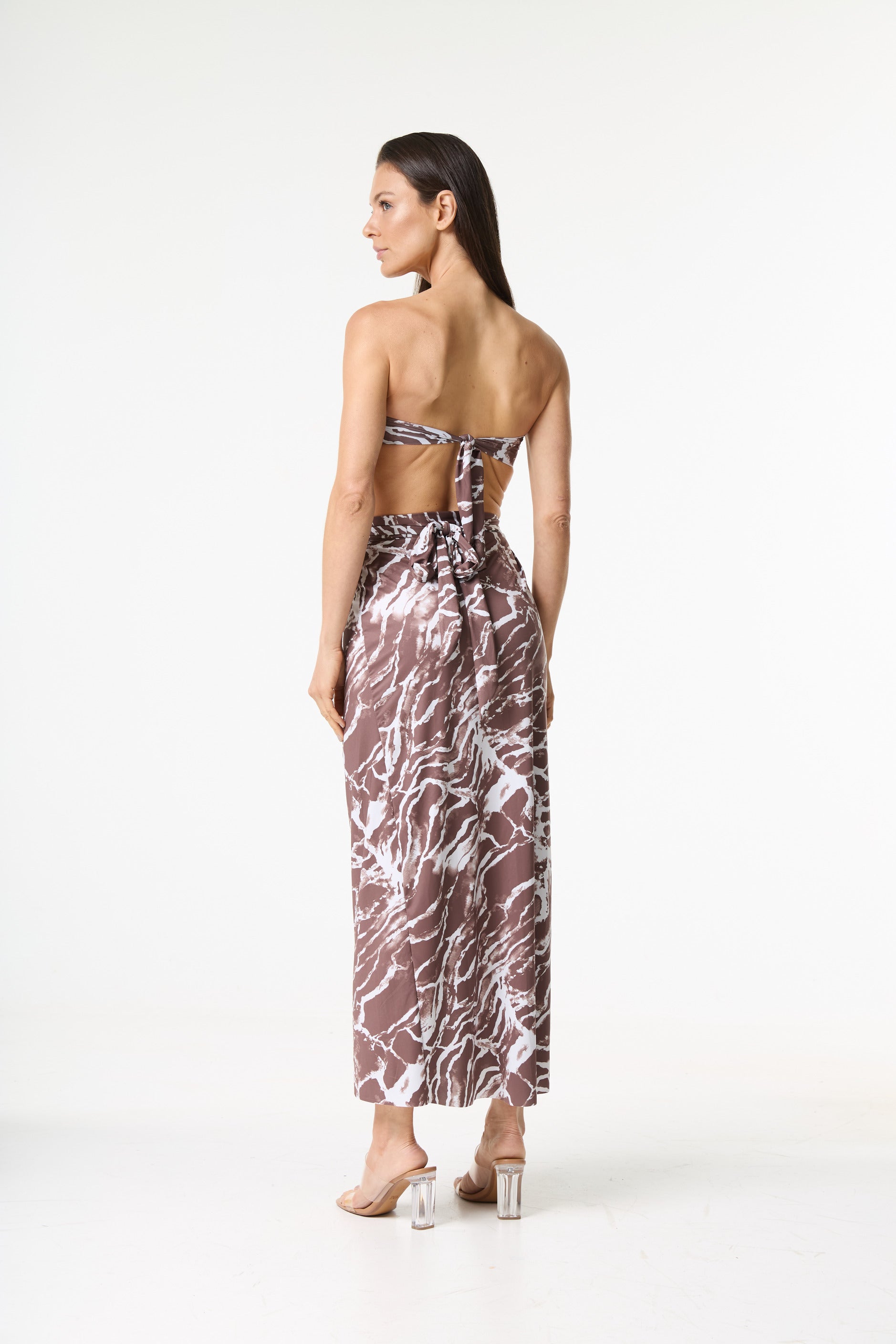 Conjunto de saída de praia com estampa marmorizada marrom e branca. A modelo é vista de costas, com a cabeça virada para o lado, mostrando o top tomara