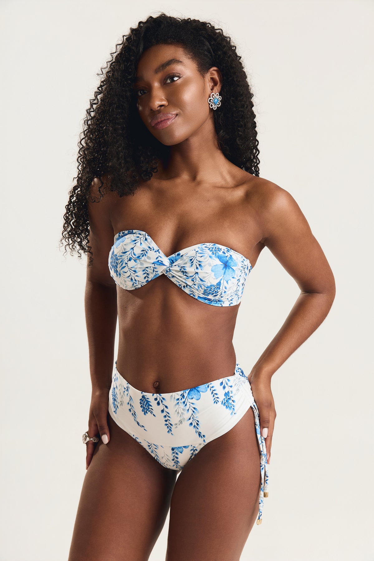 Modelo em pose frontal com mão na cintura usando top tomara que caia  e calcinha cintura alta de amarrar lateral
