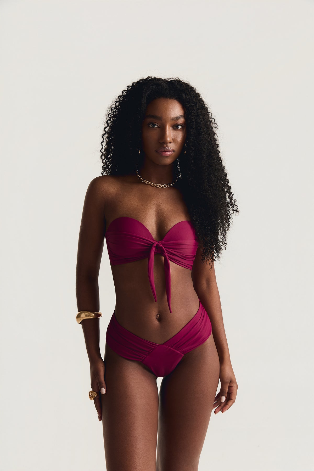 Modelo em pé de frente, com os braços ao longo do corpo, usando top tomara que caia com laço frontal e calcinha franzida na cor carmim
