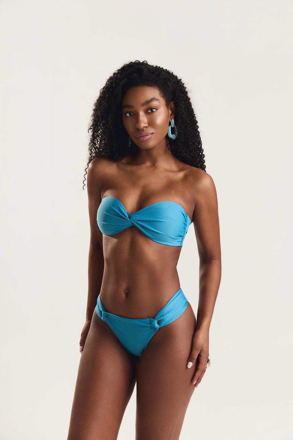 Modelo de frente usando conjunto biquíni tomara que caia azul turquesa, com top de detalhe torcido e calcinha frente dupla com nó lateral
