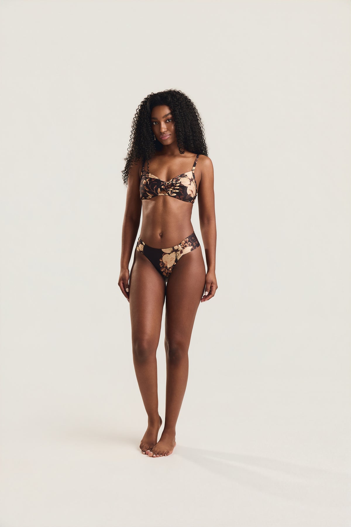 Top torcido e calcinha franzida floral preto, modelo em posição frontal com braços ao longo do corpo
