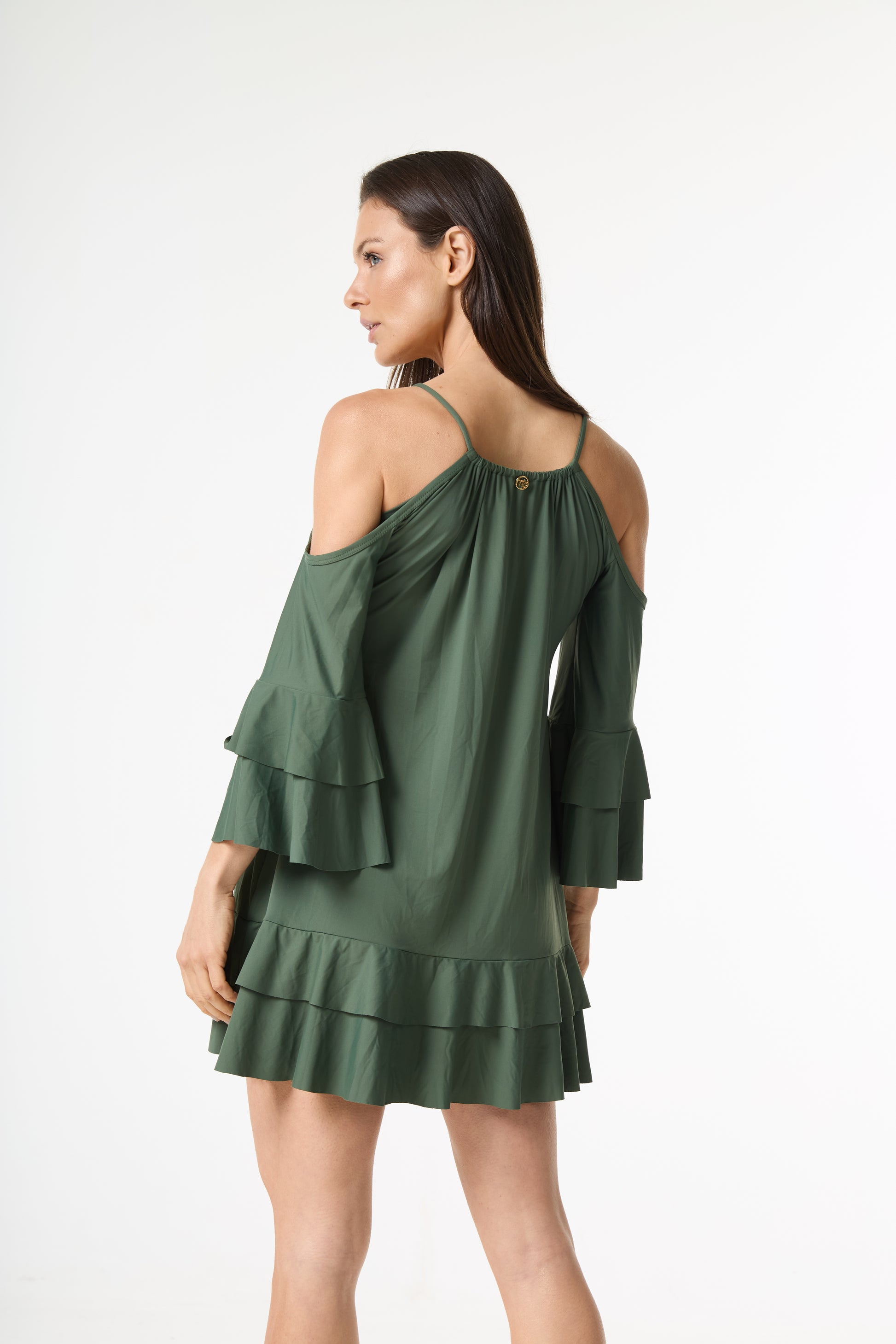 Vestido ombro a ombro verde com babados. A modelo é fotografada de costas, virando o rosto para o lado, exibindo as alças finas e o detalhe dourado na parte de trás do vestido.