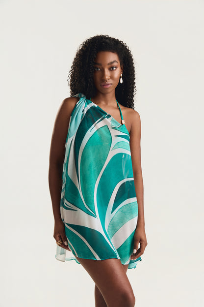 Vestido pareô estampado em geo verde, modelo de frente em posição lateral com olhar direto para a câmera, fundo neutro