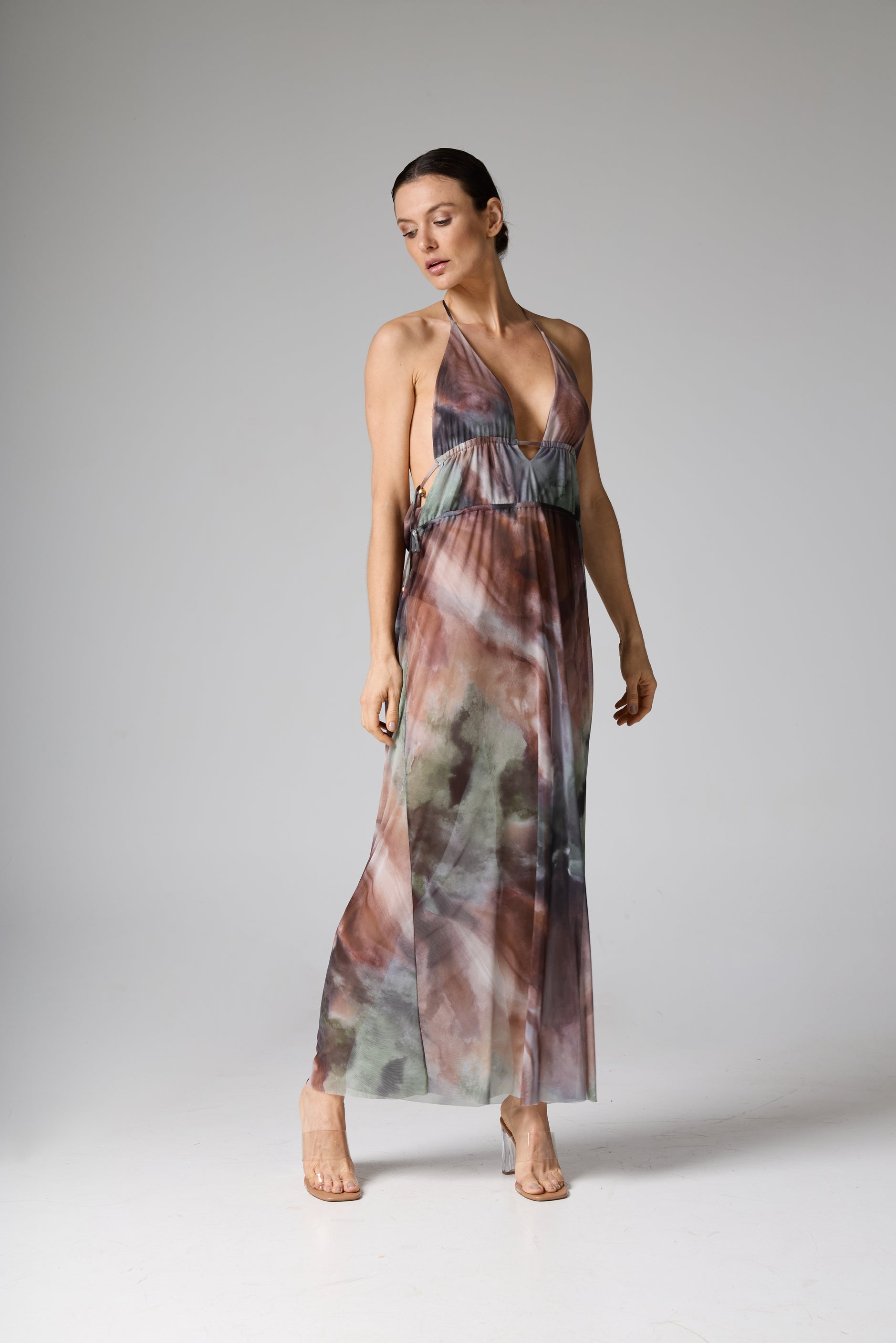 Vestido longo com decote halterneck e estampa abstrata estilo aquarela em tons de marrom, verde e cinza. A modelo está de pé, olhando para baixo.